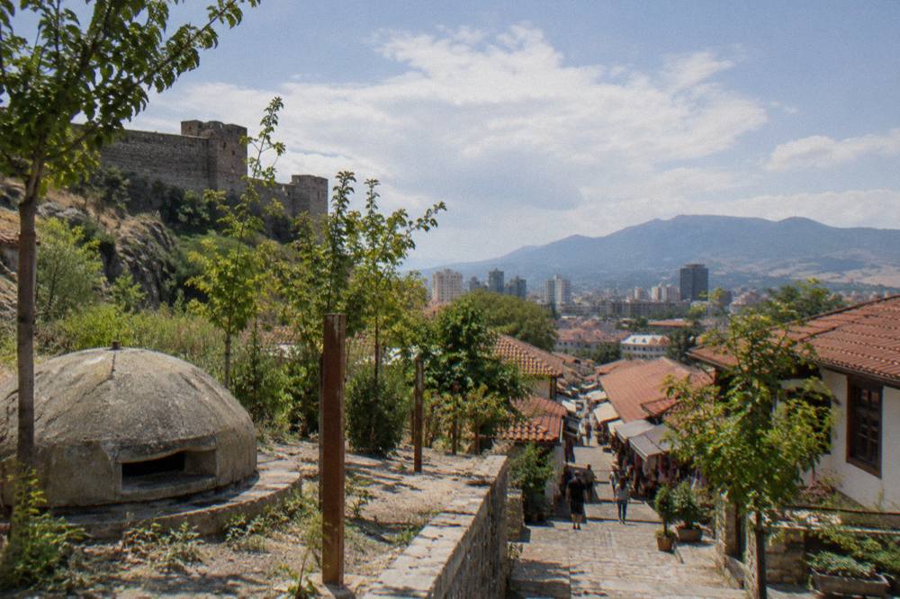 A stone castle wall on a hillside above a red-tiled old town bazaar street