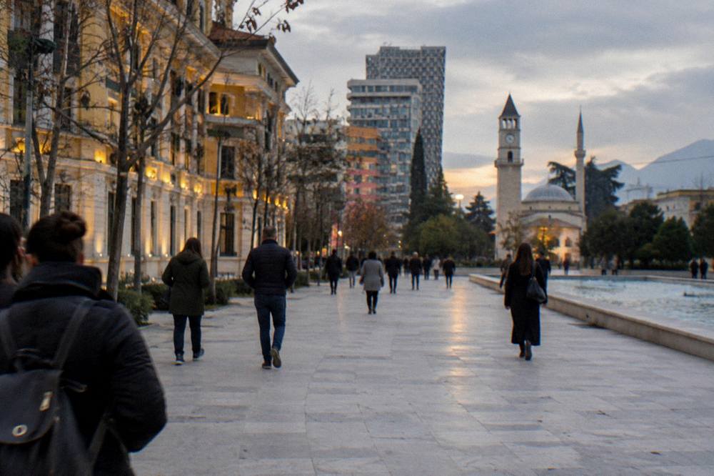 A pedestrian boulevard in central Tirana at dusk with lit facades and people walking