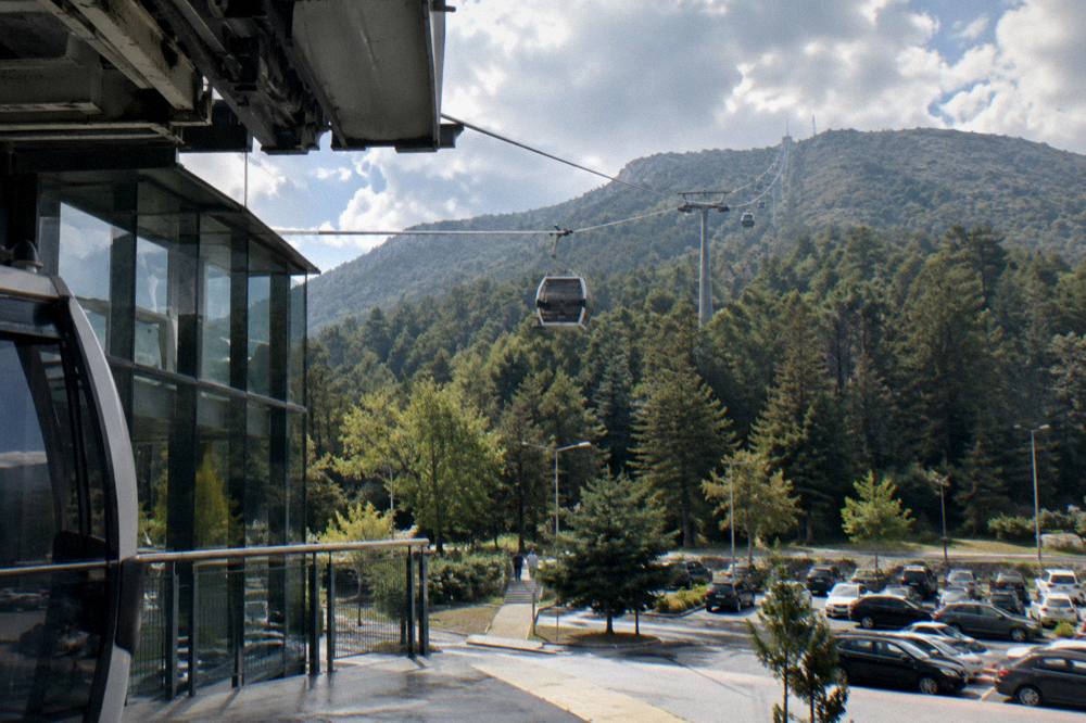A cable car cabin rising above pine trees toward the ridge of Mount Dajti