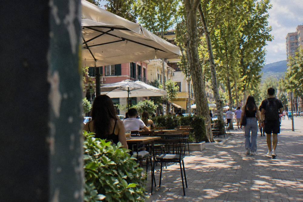 Lit cafe terraces and plane trees on an evening street in the Blloku quarter of Tirana
