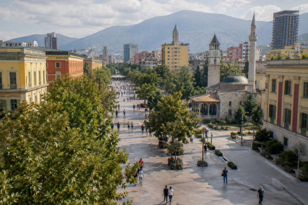 A tree-lined boulevard in central Tirana with pedestrians and colourful facades