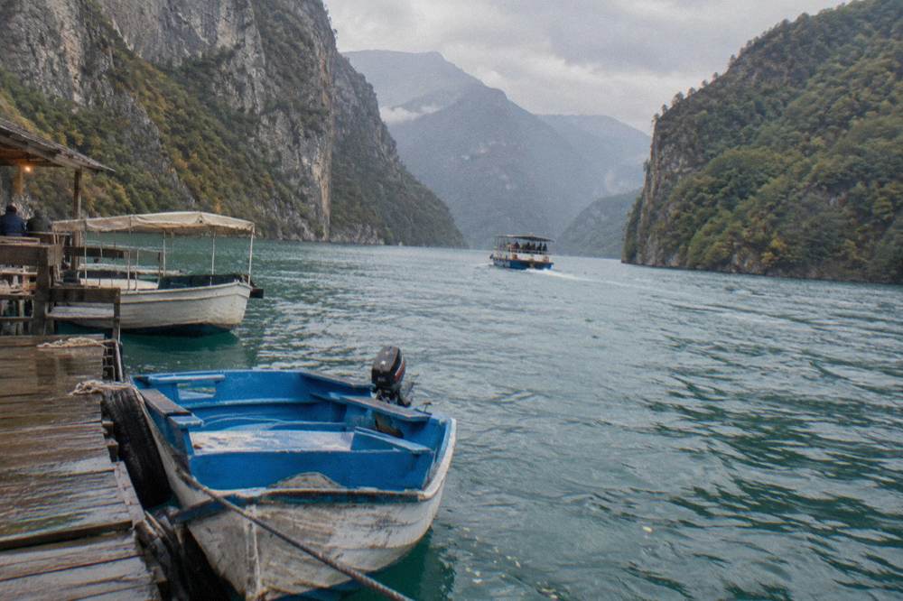 Boats moored on turquoise water at the Shala River arm of Komani lake between steep hills