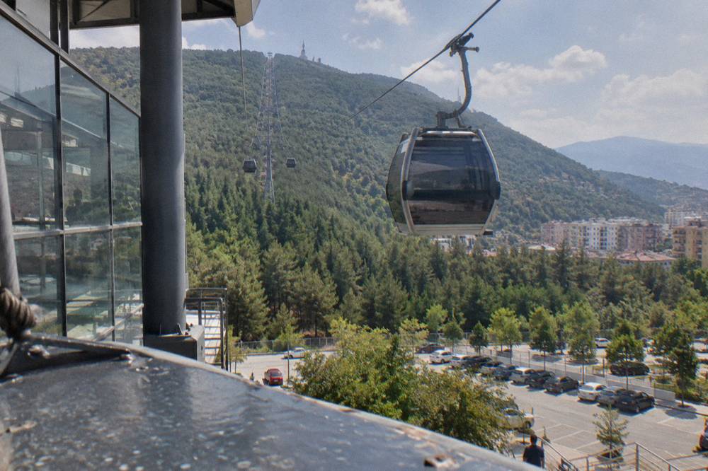 A cable car cabin rising above pine forest toward the Mount Dajti ridge above Tirana