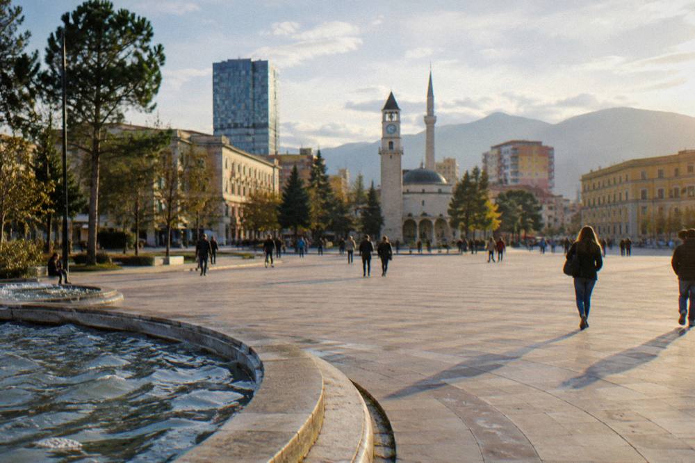 A wide tree-lined boulevard in Tirana at golden hour with mountains on the horizon