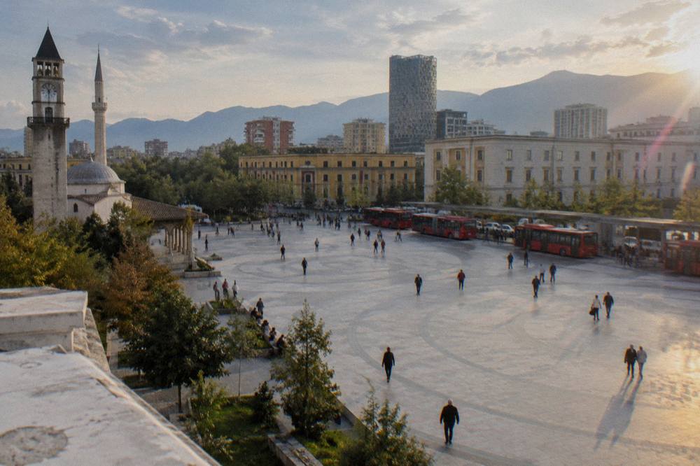 A row of red city buses waiting at a terminal on the edge of Tirana