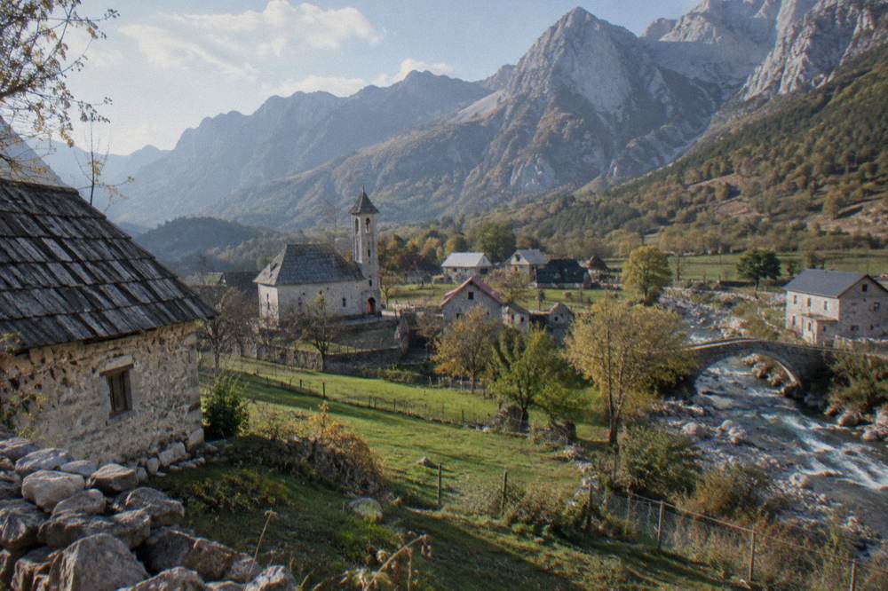 Stone houses and a church tower in the village of Theth under high peaks