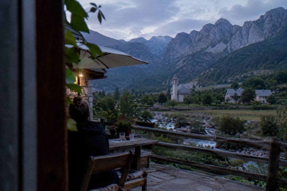 A guesthouse terrace in a mountain village with peaks behind it at dusk