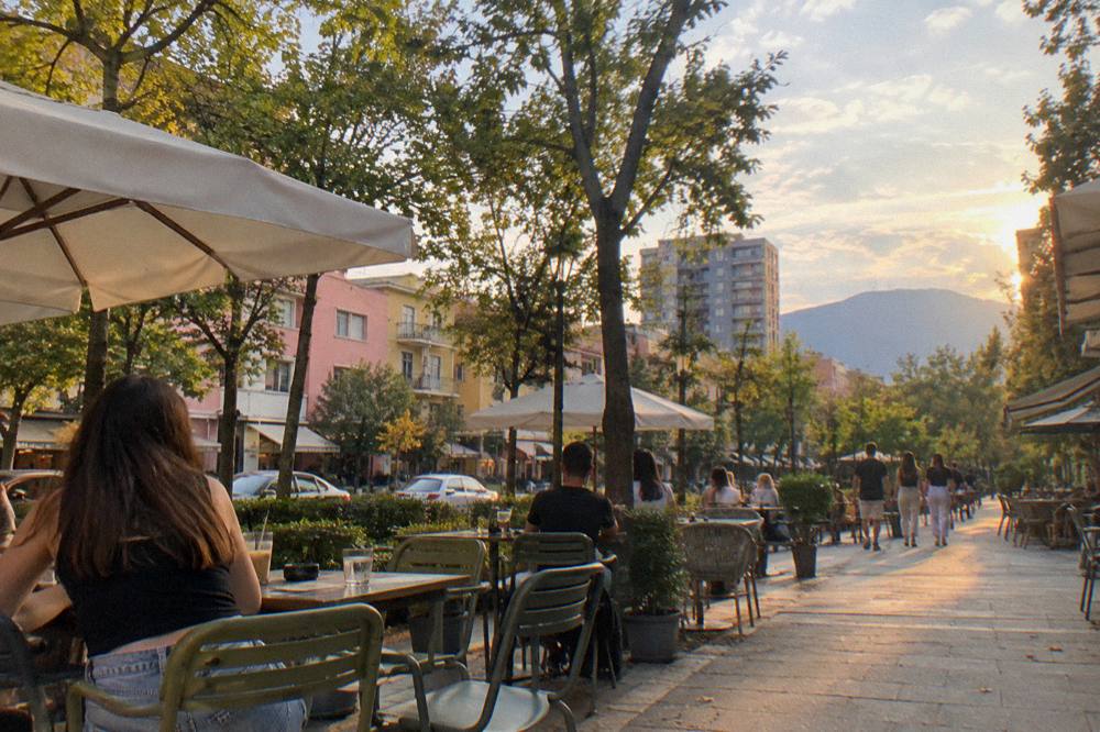 Cafe tables on a tree-lined Blloku street in Tirana in late afternoon light