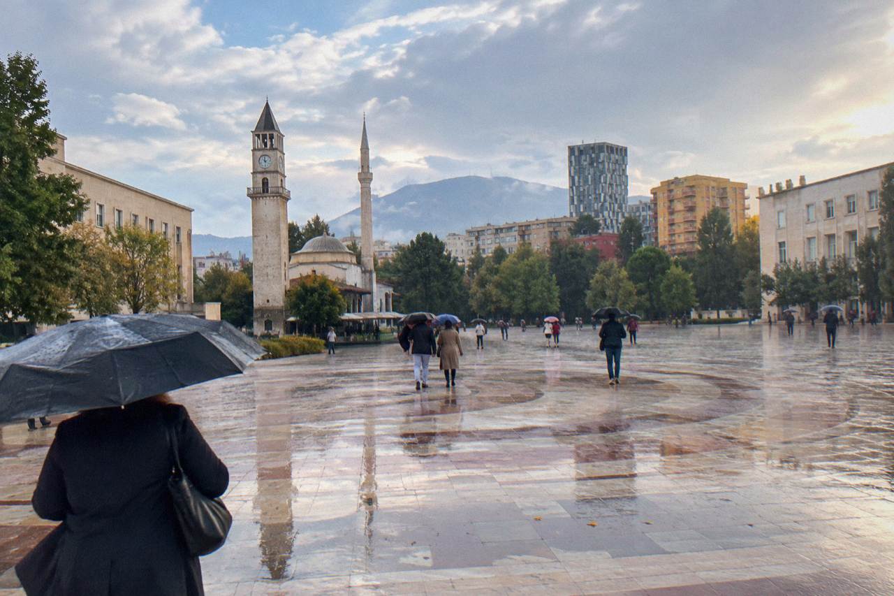 Wet cobblestones and umbrellas on a street in central Tirana with the Clock Tower in the background