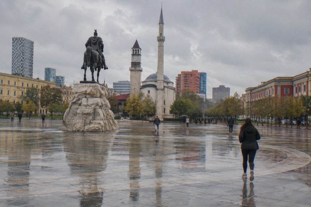 Rainy pedestrian square in Tirana with the equestrian statue and the mosque minaret behind it