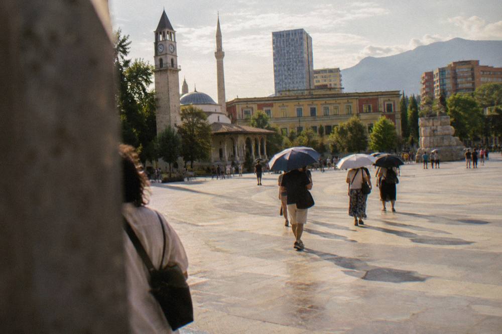 Visitors with umbrellas on a guided walk past a memorial in central Tirana