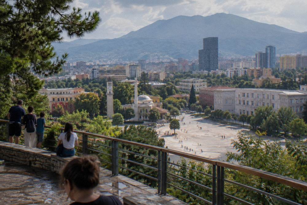 A green mountain park landscape above Tirana with a viewing terrace and families looking out over the city basin