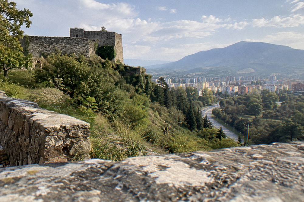 A stone castle wall on a green hill above a valley road on a clear day