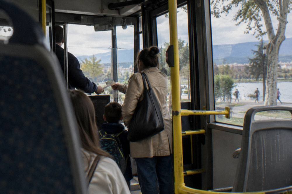A parent and child paying a bus fare in cash to a conductor on a city bus