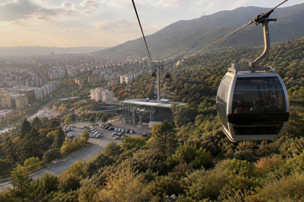 A cable car cabin rising over forest toward the Mount Dajti ridge above Tirana