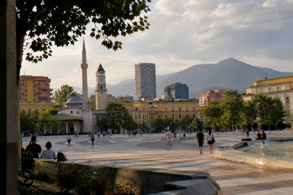 A wide cityscape of Tirana with colourful building facades and mountains behind