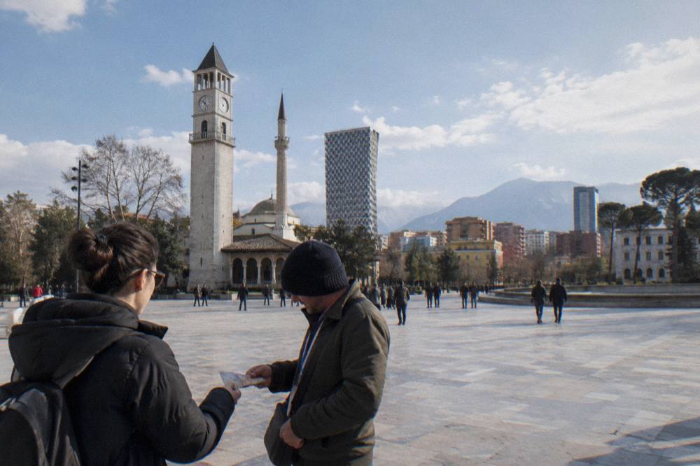 A visitor handing Albanian banknotes to a tour guide at the end of a city walk
