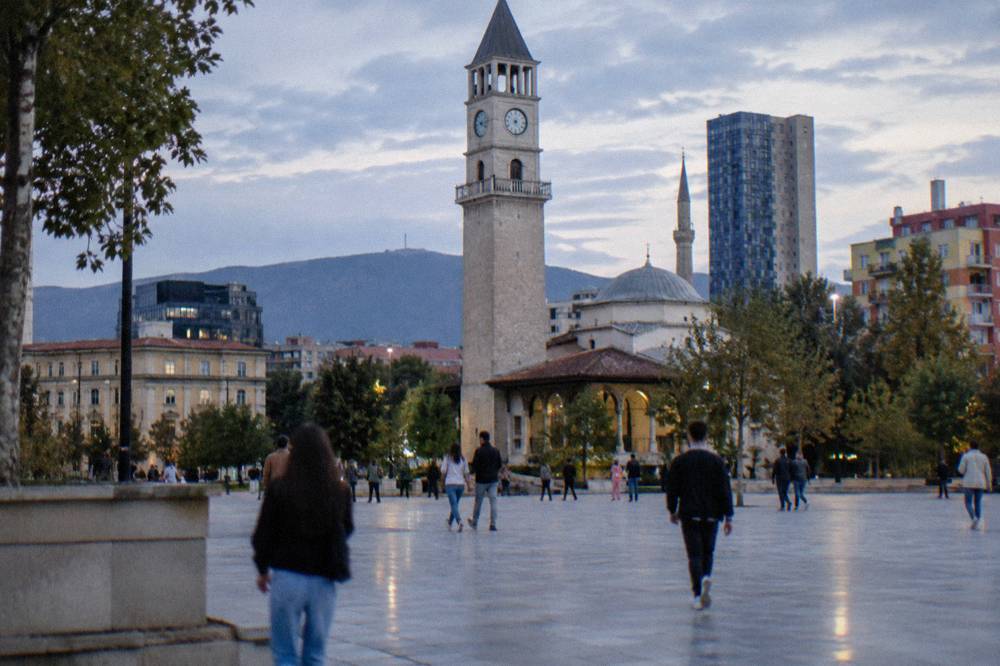 People strolling across the wide open paving of Skanderbeg Square with the Clock Tower behind