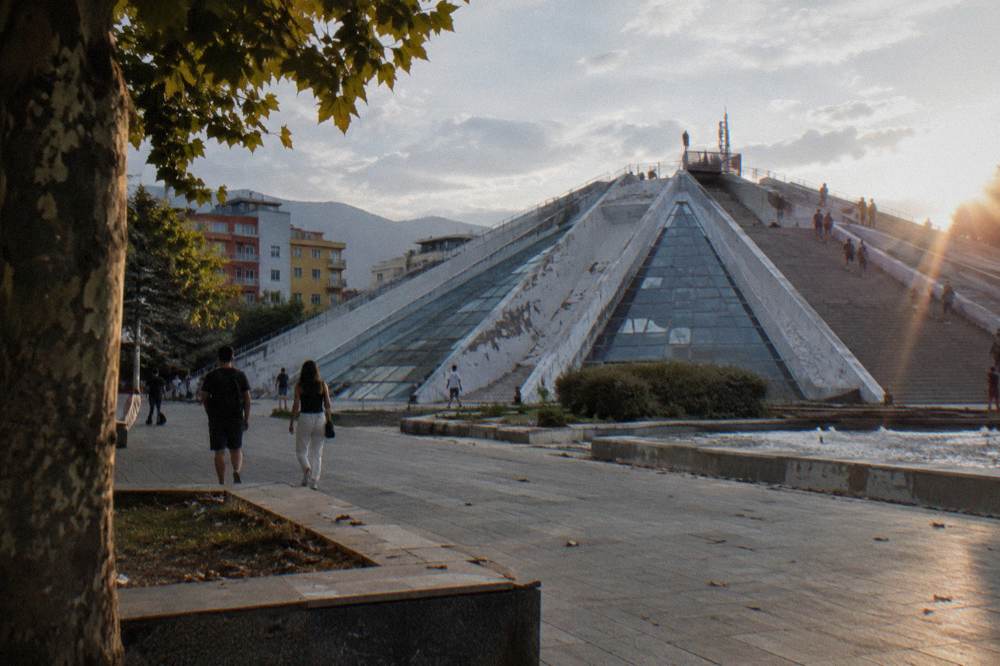 The sloped glass-clad surfaces of the Pyramid of Tirana with visitors on its steps