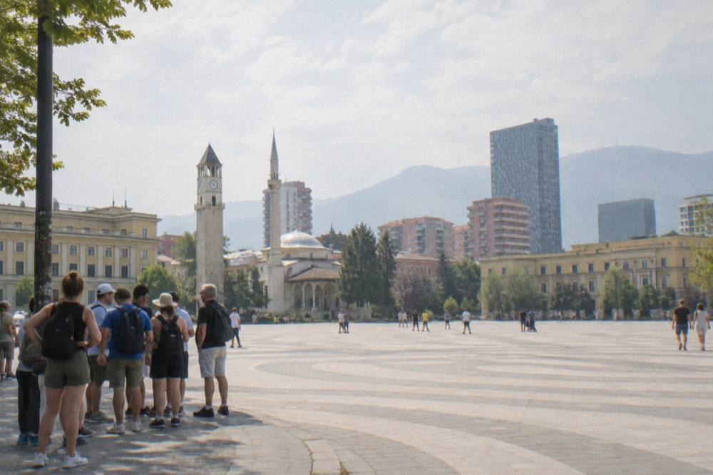 A group of tourists in trainers and daypacks gathering on a pavement corner in central Tirana