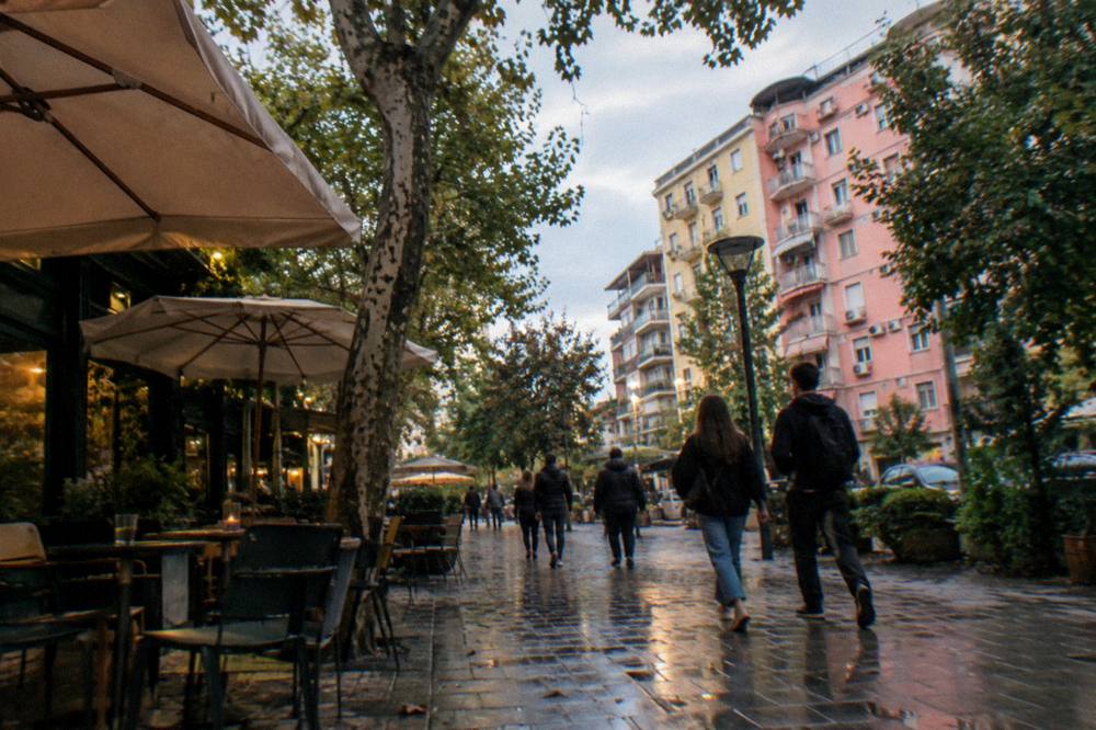 A leafy Blloku street in Tirana with cafe tables and apartment blocks in the evening