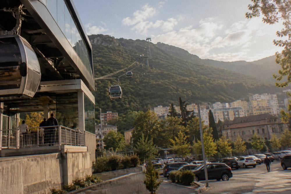 A cable car ascending a green mountain above a city skyline