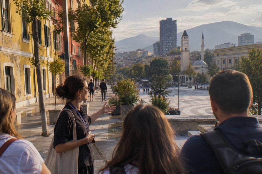 A guide speaking to a small group on a city street lined with colourful buildings