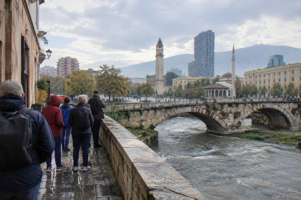 A small tour group paused on a narrow street beside an old stone bridge