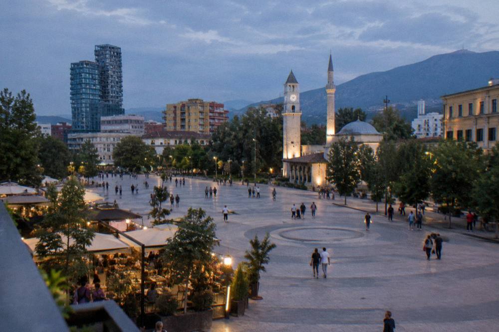 An evening street scene with lit cafe terraces and people strolling